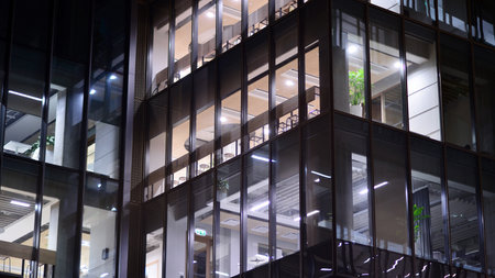 Office building in the evening with lightened workspaces. Modern, glazed skyscraper in financial district. Late hours in the office.の写真素材