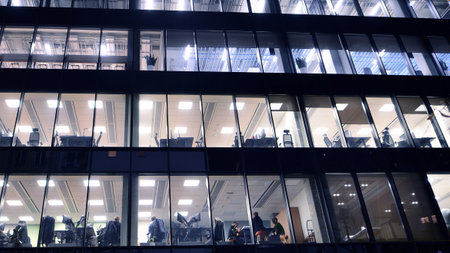 Office building in the evening with lightened workspaces. Modern, glazed skyscraper in financial district. Late hours in the office.の写真素材