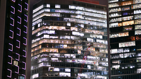 Office building in the evening with lightened workspaces. Modern, glazed skyscraper in financial...