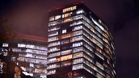 Office building in the evening with lightened workspaces. Modern, glazed skyscraper in financial district. Late hours in the office.の写真素材