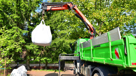 Crane with a big bag of stones. It is a white big bag with decorative stones for the property.の写真素材