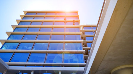 Modern office building with glass facade. Transparent glass wall of office building. Reflection of the blue sky on the facade of the building.の写真素材