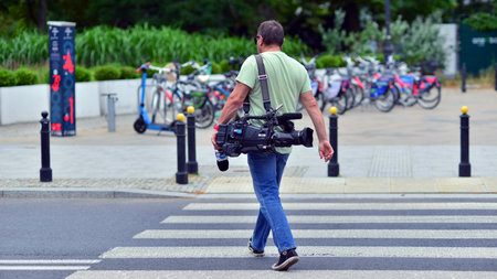 Warsaw, Poland. July 8, 2025. A cameraman holding professional filming equipment walk street.