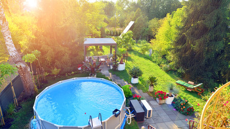 Garden of a suburban house in summer in which you can see a removable swimming pool, pergola in a...