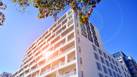 A residential building by lush green trees and surrounded by fresh vegetation on a clear sunny day. Modern architecture residential apartment building complex surrounded by greenの写真素材