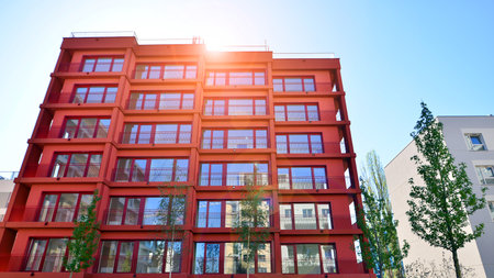 A residential building by lush green trees and surrounded by fresh vegetation on a clear sunny day. Modern architecture residential apartment building complex surrounded by greenの写真素材