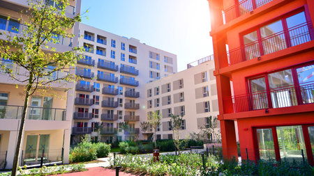 A residential building by lush green trees and surrounded by fresh vegetation on a clear sunny day....