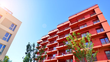 A residential building by lush green trees and surrounded by fresh vegetation on a clear sunny day....