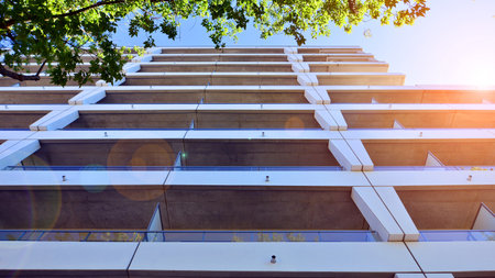 A residential building by lush green trees and surrounded by fresh vegetation on a clear sunny day....