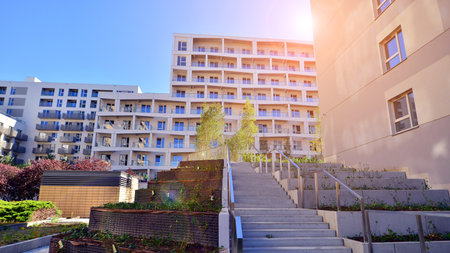 A residential building by lush green trees and surrounded by fresh vegetation on a clear sunny day....