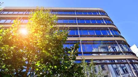 Glass office building surrounded with green trees. Eco-friendly office building. Sustainable...