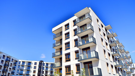 A residential building by lush green trees and surrounded by fresh vegetation on a clear sunny day. Modern architecture residential apartment building complex surrounded by greenの写真素材