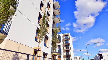 A residential building by lush green trees and surrounded by fresh vegetation on a clear sunny day....