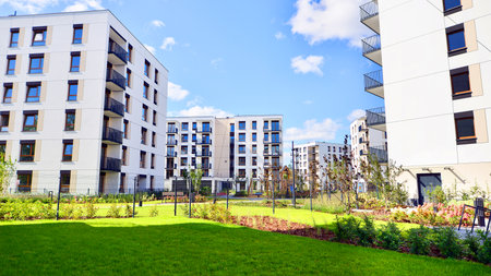 A residential building by lush green trees and surrounded by fresh vegetation on a clear sunny day. Modern architecture residential apartment building complex surrounded by greenの写真素材