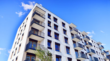 A residential building by lush green trees and surrounded by fresh vegetation on a clear sunny day....