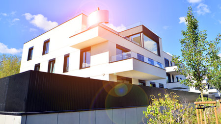 Modern apartment building with balconies and greenery. The structure features a glass wall and lush plants in front, showcasing contemporary architecture.の写真素材