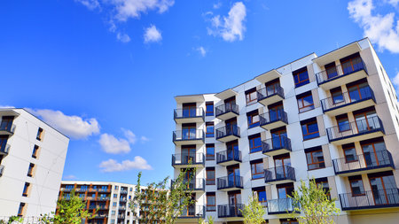 A residential building by lush green trees and surrounded by fresh vegetation on a clear sunny day....