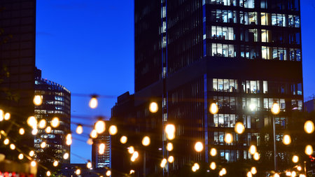In night the foreground abstract blurred garlands. In the background modern glass office building. Rows of lit windows out the architectural grid of a modern facade.の写真素材