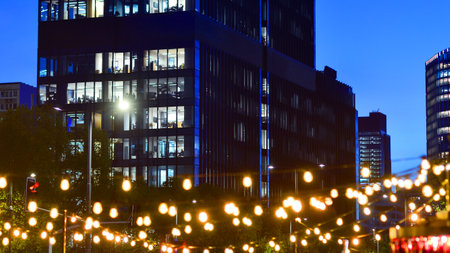 In night the foreground abstract blurred garlands. In the background modern glass office building. Rows of lit windows out the architectural grid of a modern facade.の写真素材