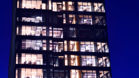 Modern office building in city center illuminated at night. Rows of lit windows against the architectural grid of a modern facade. Concrete and glass facade in its night version.の写真素材