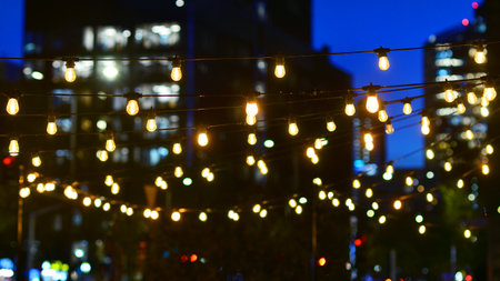 Light bulbs garlands against glass modern buildings background in night. Blurred rows of lit windows...