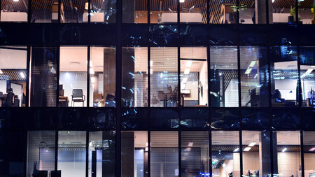 Modern office building in city center illuminated at night. Rows of lit windows against the architectural grid of a modern facade. Concrete and glass facade in its night version.の写真素材