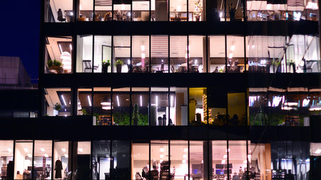 Modern office building in city center illuminated at night. Rows of lit windows against the architectural grid of a modern facade. Concrete and glass facade in its night version.の写真素材
