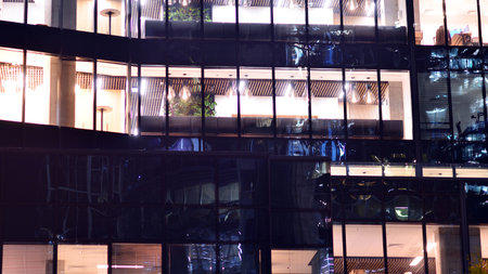 Modern office building in city center illuminated at night. Rows of lit windows against the architectural grid of a modern facade. Concrete and glass facade in its night version.の写真素材