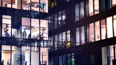 Modern office building in city center illuminated at night. Rows of lit windows against the architectural grid of a modern facade. Concrete and glass facade in its night version.の写真素材