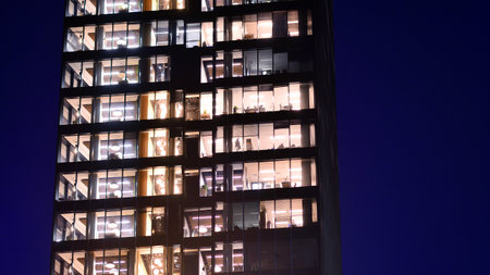 Modern office building in city center illuminated at night. Rows of lit windows against the architectural grid of a modern facade. Concrete and glass facade in its night version.の写真素材