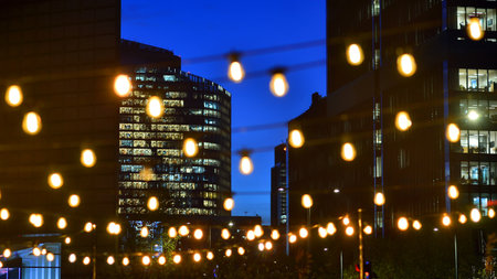 In night the foreground abstract blurred garlands. In the background modern glass office building. Rows of lit windows out the architectural grid of a modern facade.の写真素材