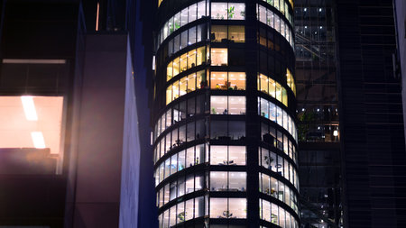 Modern office building in city center illuminated at night. Rows of lit windows against the architectural grid of a modern facade. Concrete and glass facade in its night version.の写真素材
