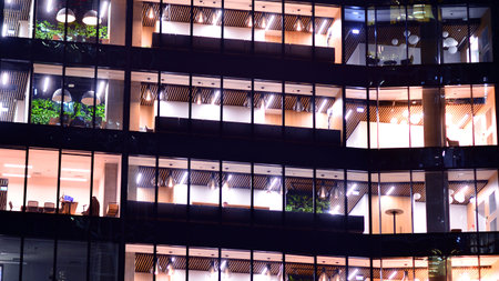 Modern office building in city center illuminated at night. Rows of lit windows against the architectural grid of a modern facade. Concrete and glass facade in its night version.の写真素材