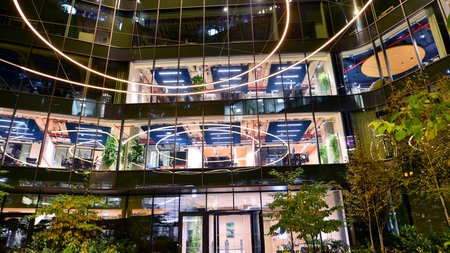 Modern office building in city center illuminated at night. Green trees near a modern office...