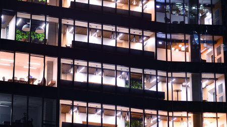Modern office building in city center illuminated at night. Rows of lit windows against the architectural grid of a modern facade. Concrete and glass facade in its night version.の写真素材
