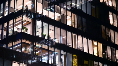 Modern office building in city center illuminated at night. Rows of lit windows against the...