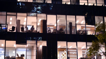 Modern office building in city center illuminated at night. Rows of lit windows against the architectural grid of a modern facade. Concrete and glass facade in its night version.の写真素材