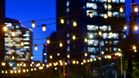 Light bulbs garlands against glass modern buildings background in night. Blurred rows of lit windows...