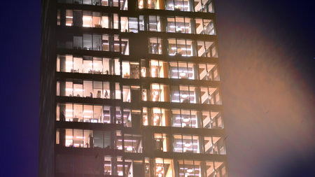 Modern office building in city center illuminated at night. Rows of lit windows against the architectural grid of a modern facade. Concrete and glass facade in its night version.の写真素材