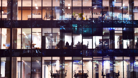 Modern office building in city center illuminated at night. Rows of lit windows against the architectural grid of a modern facade. Concrete and glass facade in its night version.の写真素材