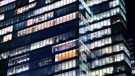 Modern office building in city center illuminated at night. Rows of lit windows against the...