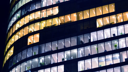 Modern office building in city center illuminated at night. Rows of lit windows against the...