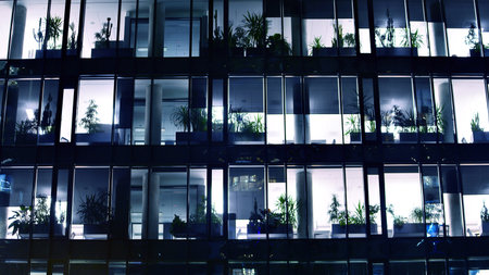 Modern office building in city center illuminated at night. Rows of lit windows against the architectural grid of a modern facade. Concrete and glass facade in its night version.の写真素材