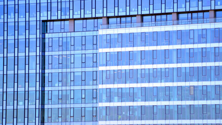 Structural glass wall reflecting blue sky. Abstract modern architecture fragment. Glass building with transparent facade of the building and blue sky.の写真素材