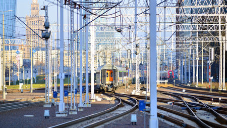Warsaw, Poland. 28 November 2025. A passenger train on the tracks near the station. Tracks, electrical wires and metal masts against the backdrop of a city skyscrapers on a winterのeditorial素材