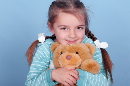 Smiling child girl holding teddy bear over blueの写真素材