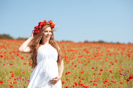 Smiling pregnant woman wearing floral wreath in poopy field. Resting outdoors.の写真素材
