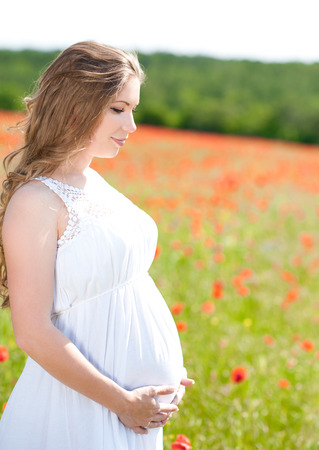 Pregnant girl holding belly outdoors. Posing in poppy field. Motherhood.の写真素材