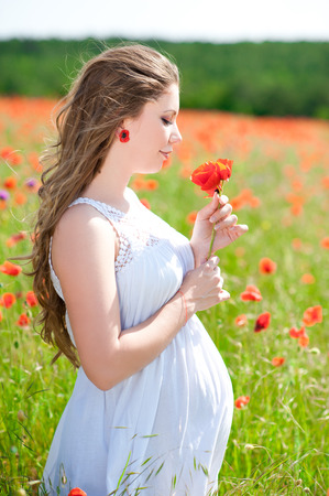 Pregnant woman smelling flower outdoors. Resting in poppy field. Motherhood. Maternityの写真素材