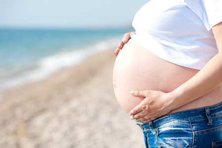 Pregnant woman holding belly over sea. Resting outdoors. Motherhood. Maternity.の写真素材